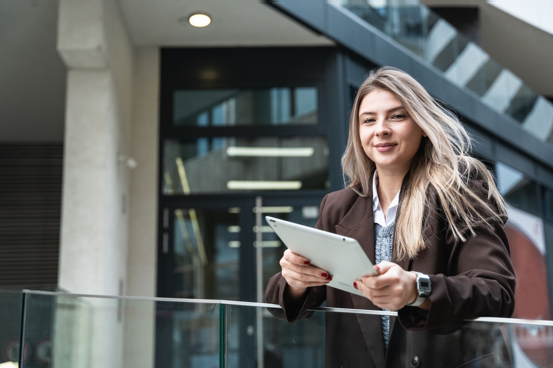 Young business woman freelance motivational speaker life coach standing in front of office building with digital tablet preparing for staff meeting. Businessperson product strategy expert waiting