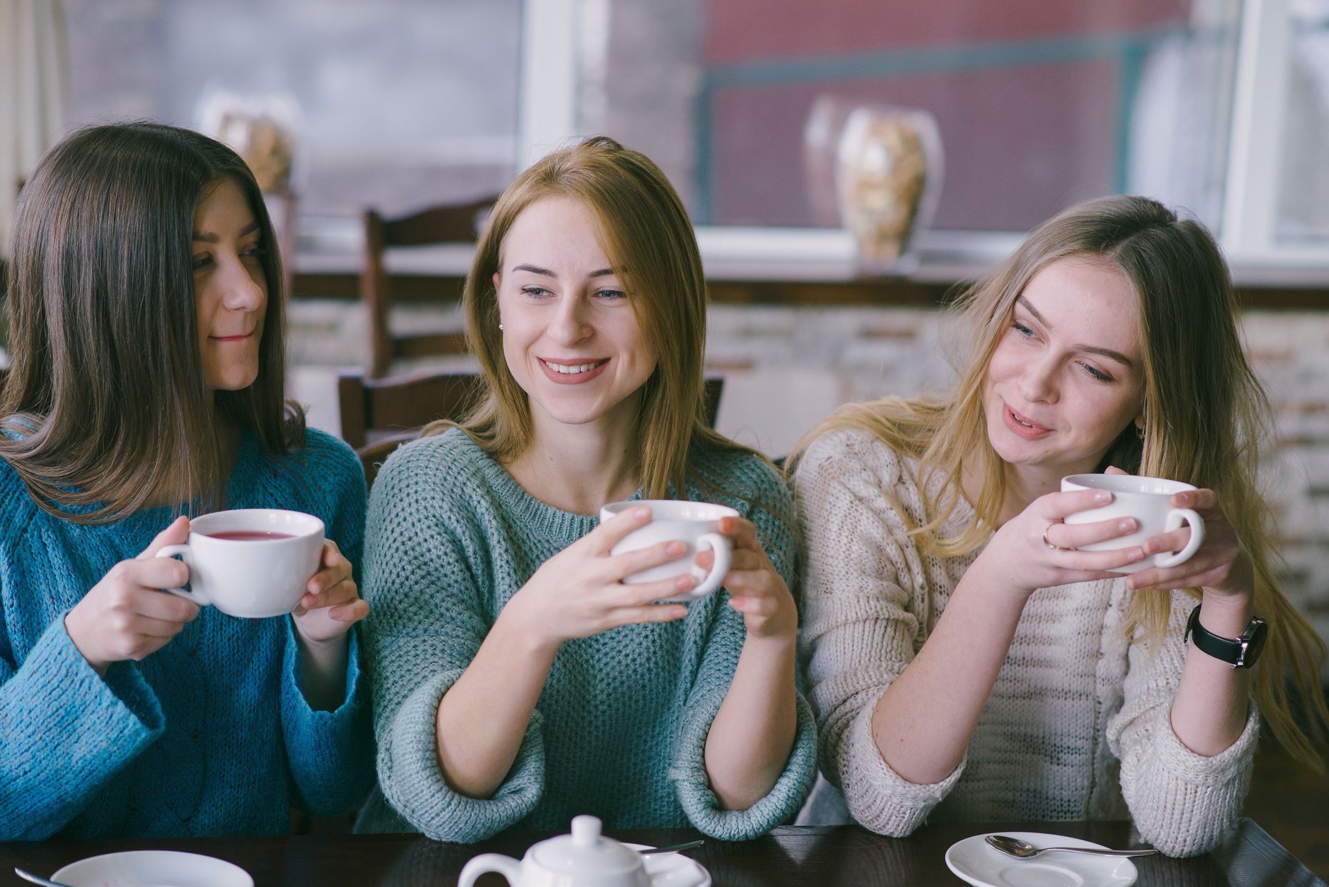 three girls sitting in a cafe at the table and drink tea